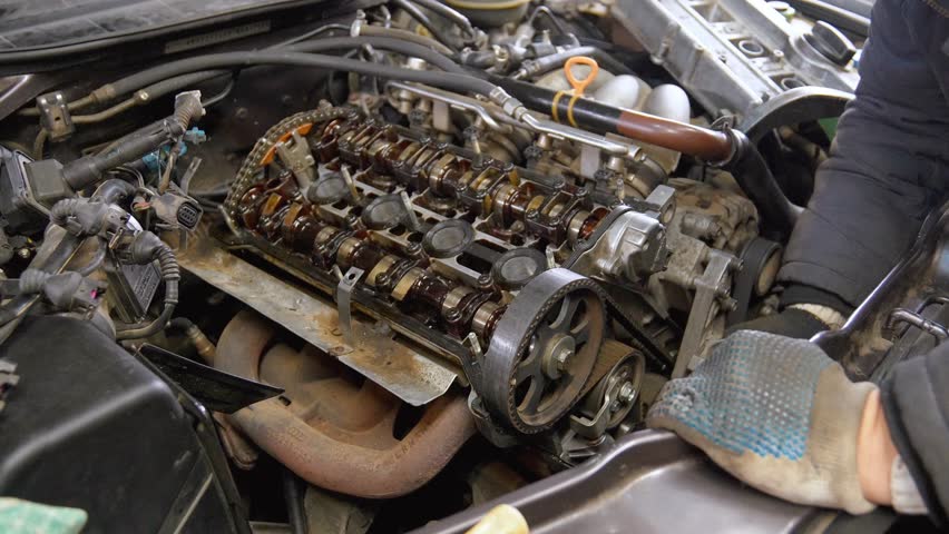Car mechanics remove valve cover from engine, accessing cylinder head for servicing and replacing valve cover gasket during routine maintenance and repair work