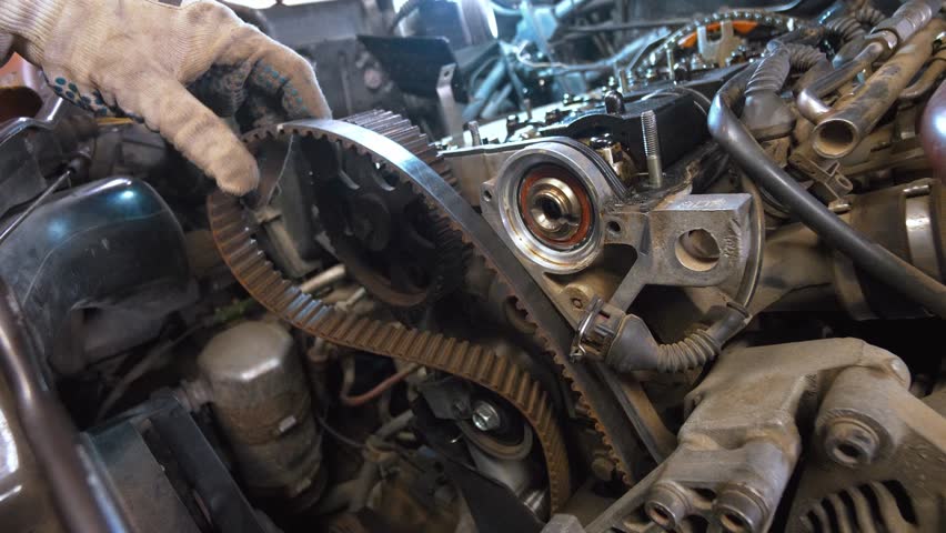Mechanic in gloves points to worn timing belt on car engine, highlighting signs of damage and need for replacement during routine and repair work