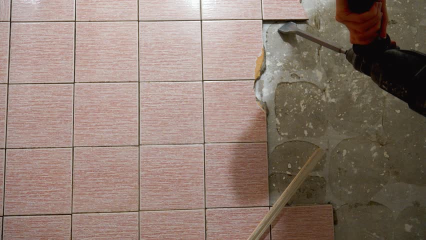 Builders remove old floor tiles with chisel, perforator and hammer, preparing surfaces for repair. Dust and debris accumulate in process of transforming spaces