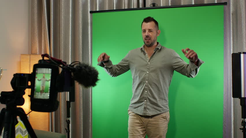 Man confidently presenting in a studio setup with green screen and casual attire