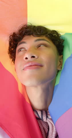 Vertical video: Smiling person wrapped in rainbow flag, embracing pride and joy at home. LGBTQ, happiness, celebration, freedom, inclusivity, community