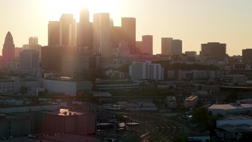 Aerial rising facing industry of downtown Los Angeles during sunset as sun rays glow between buildings