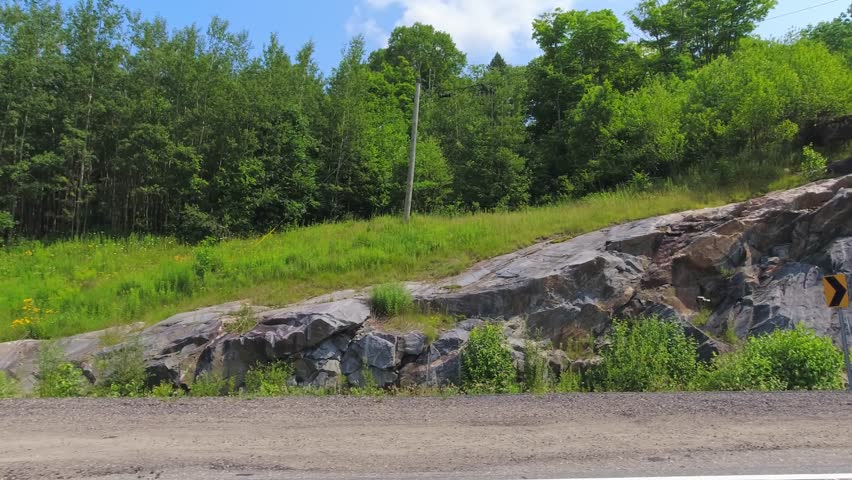 Point of view, right side car view. Passenger window side driving view, POV driving on Highway 11. Roads of Canada with scenic road with rock walls and green trees. Canadian Shield. Car movie backing