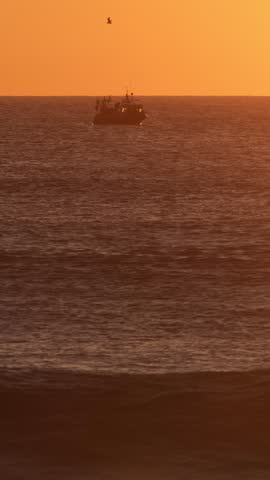 Fishing boat silhouette in ocean on sunset with waves. Costa da Caparica, Portugal