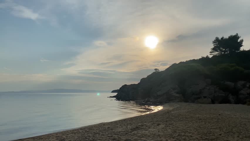 the sun through the clouds in the sky over the sea from behind the mountain