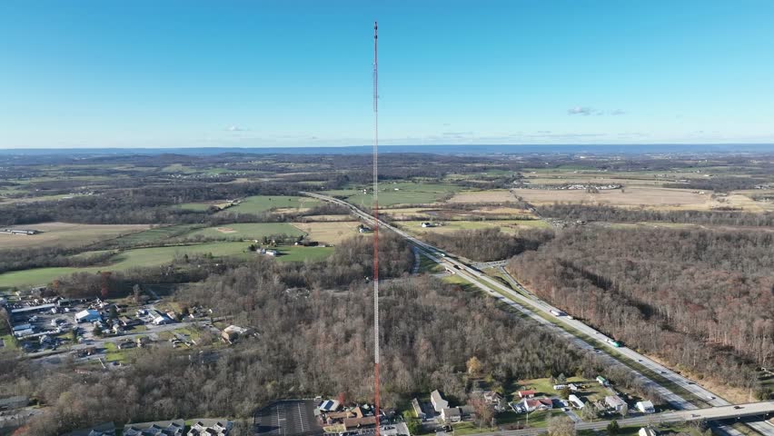 High transmission tower in rural area of American town. Countryside with housing area in suburb. Sunny day in fall season. Aerial orbit wide shot.