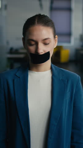 Vertical Screen: Young woman in a business setting removes tape from her mouth, smiling confidently afterward. Concept of overcoming silence, freedom of expression, and empowerment in the workplace