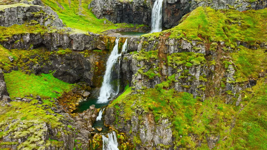 Wispy waterfalls flowing over cliff, Mountain river falling over cliff creating many waterfalls with green vegetation in Iceland 