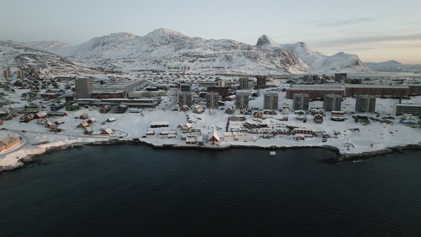 Drone shot over Nuuk, Greenland, in January 2025. Waterfront with colorful houses, snow-covered streets, cars, and mountains in the background near the Hans Egede statue. 