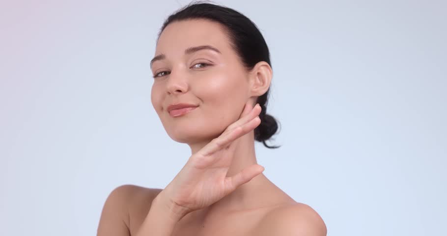 Close-up of a young woman with glowing skin smiling while gently touching her face. Perfect for skincare concepts, beauty products promotion, and self-care campaigns. 