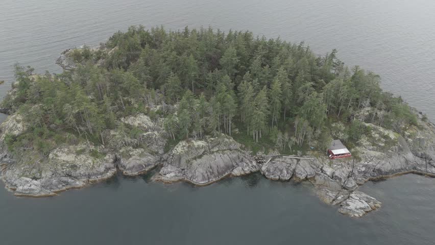 An aerial footage of a an islet covered with green vegetation off the Sunshine Coast on a cloudy day in Gibsons town, British Columbia, Canada