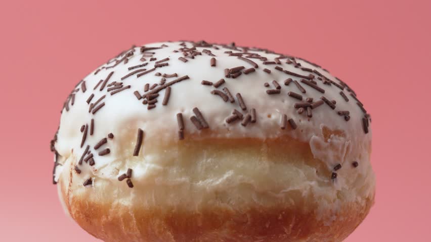 A donut with sprinkles on top. The sprinkles are brown and white. The donut rotates on a pink background.