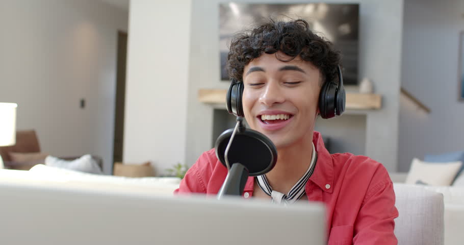 Wearing headphones, transgender teenage boy smiling and recording podcast at home. Podcasting, home studio, broadcasting, audio, microphone, lifestyle