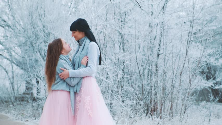 happy family mother and daughter posing for photo shoot, woman hugs little girl with love care, two people together. Winter nature forest trees frost, white snow. Same clothes gray sweater pink dress