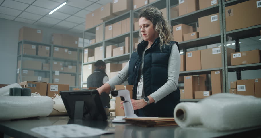 Female Postal Worker, Shipping Clerk Packs Cardboard Parcel with E-Commerce Order, Prepares Package for Delivery to Client, Uses Tablet Computer. Warehouse Facility, Sorting Center of Postal Service.