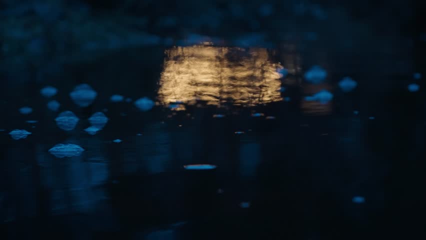 Lights of Illuminated wooden cottage in the middle of a forest by the river reflected in the water at autumn night