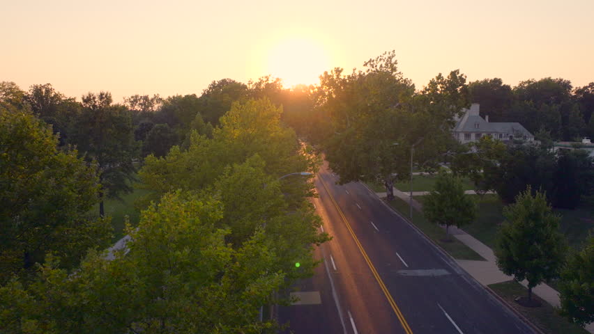 Aerial of Lindell Blvd in Forest Park neighborhood of St. Louis, Missouri at sunset with a rise above the trees to reveal downtown Clayton city skyline and the sun on a beautiful evening in summer.