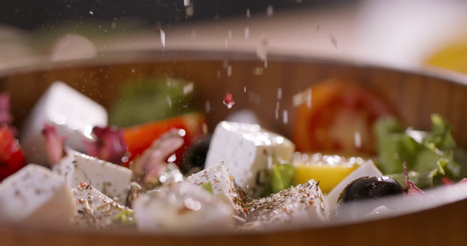 A Bowl of Vibrant Mediterranean Greek Salad with Feta Cheese Being Seasoned with Natural Ingredients, Emphasizing Wellness, Balanced Diet, and Fresh Culinary Artistry