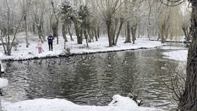 A mother and daughter feed ducks in a snowy park. The ducks swim in the water, enjoying the food. - Powered by Shutterstock - Get 15% off with code: PIKWIZARD15