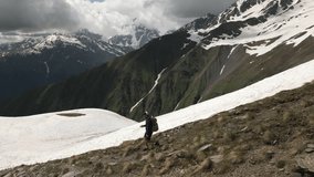Aerial of solo hiker in high mountains with snow-capped peaks. Man walks with backpack through rocky terrain. Winter adventure in wilderness. Trekking, exploration, remote trail. - Powered by Shutterstock - Get 15% off with code: PIKWIZARD15