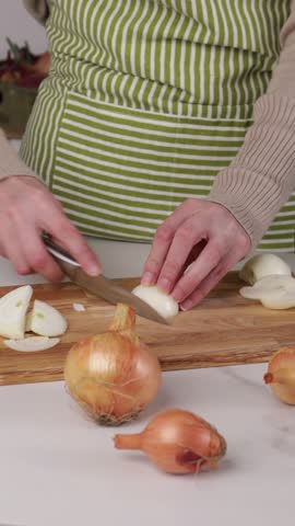 hands slicing onion bulb on cutting board for soup
