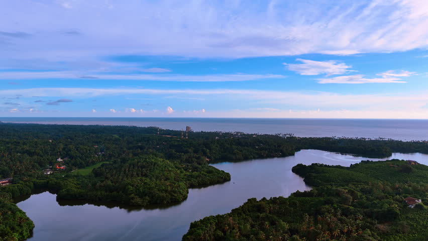 Wavy river flowing among the green banks and into the Indian Ocean. Stunning azure sky with light clouds at backdrop. Sri Lanka nature.