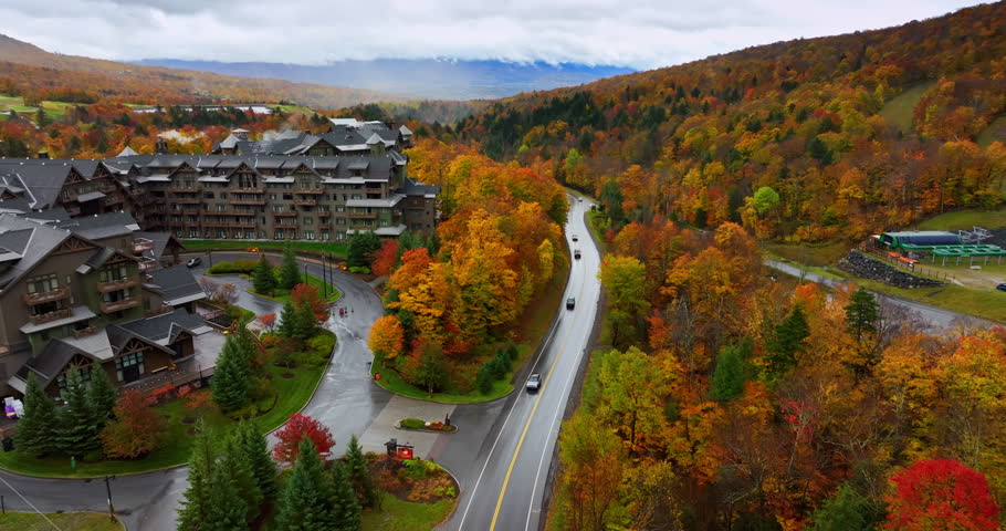 Amazing bright autumn colors in the scenery of Vermont, New England, USA. Flight over the road near the beautiful cottages at the mountain foot. Aerial view.