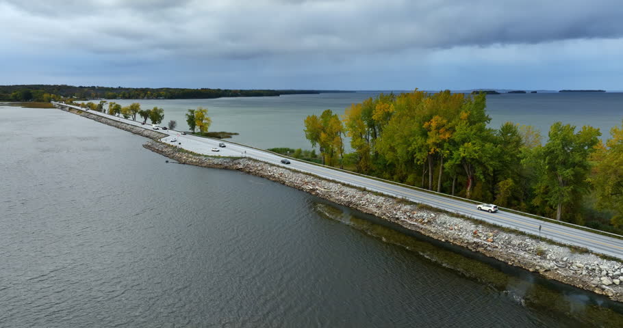 Cars riding by the highway built along the lake. Waterscape of Lake Champlain, Vermont, New England, USA. Grey day on the lake.