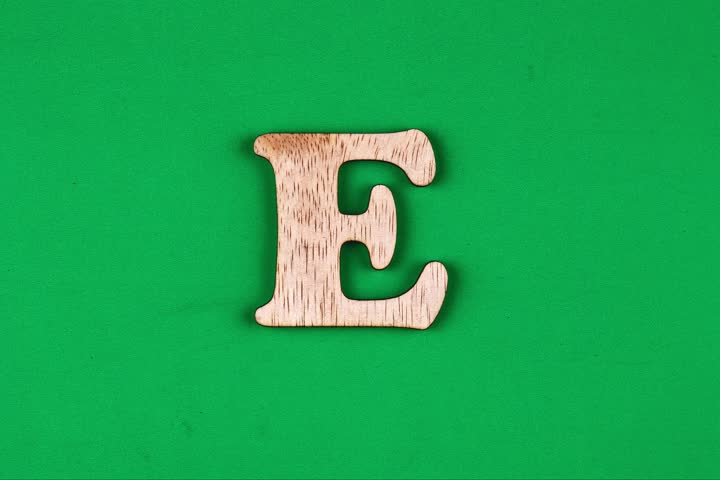 A single, capital letter "E" crafted from light brown wood is positioned against a solid, bright green backdrop.
