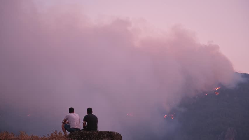 Desperate People Watching the Fire in the Forest Forest fire near a town burns through mountain slopes.Firefighters in safety gear work tirelessly to extinguish the flames.