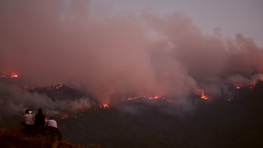 Desperate People Watching the Fire in the Forest Forest fire near a town burns through mountain slopes.Firefighters in safety gear work tirelessly to extinguish the flames.