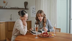 Two women reading magazine in modern kitchen at friendly gathering closeup. Stylish girl flipping periodical pages showing fashion looks to female friend. Couple ladies enjoy home meeting with wine. - Powered by Shutterstock - Get 15% off with code: PIKWIZARD15