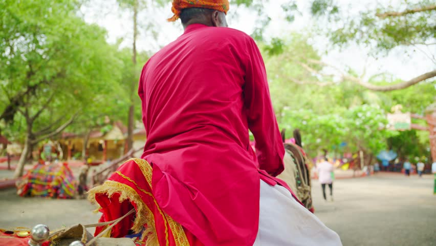 Elderly man rides decorated horse in traditional clothes, Old person dressed as cultural clothing, Sits on Ornamented steed, Villager smiles while mounted Colt through rural area, Festive decorations