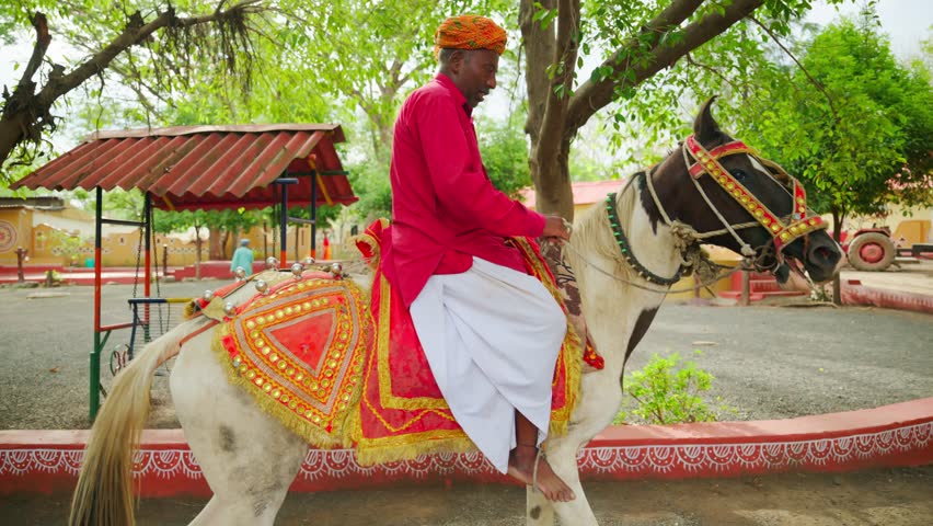 Aged man in traditional wear rides on decorated horse, Old man with heritage attire riding a Ornamented steed, Lively village road, Festive season, Colorful Rural path, Regional dress, Decoration area