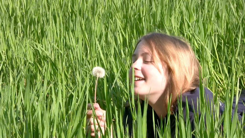 Teen girl lying in a bright green grass with dandelion in his hand. Laughter