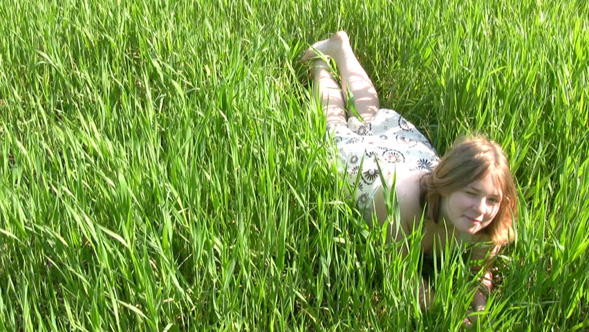 Bright sunny day. Teen girl in a light dress rolled in lush green grass