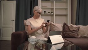 Old woman sitting on a couch with a tablet, listening to music with headphones, learning digital technology in a cozy home environment  - Powered by Shutterstock - Get 15% off with code: PIKWIZARD15