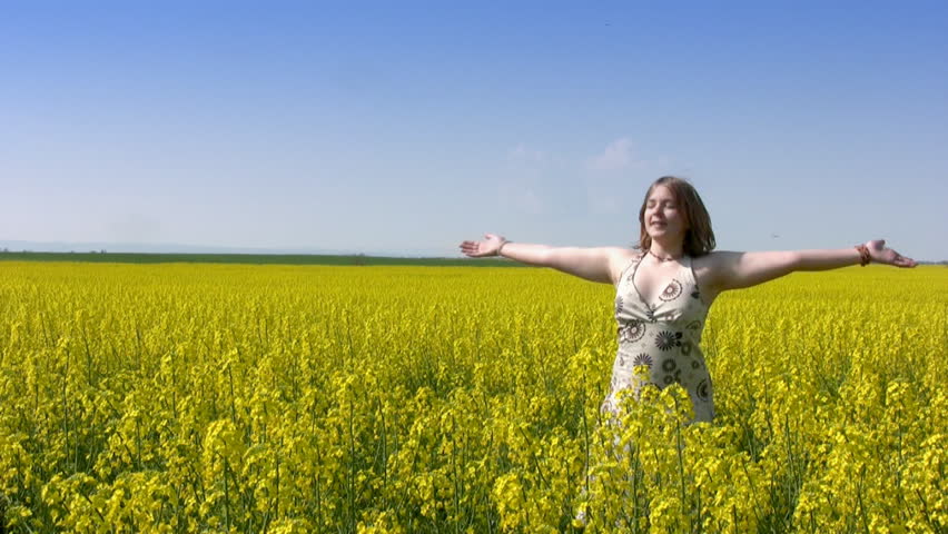 Teen girl closed her eyes and spins with his arms raised in a field of canola.