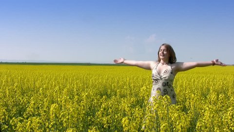 Teen girl closed her eyes and spins with his arms raised in a field of canola. Clear sunny skies. A vast field of yellow flowers. Dizzy and girl fell into the soft grass