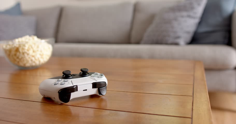 Video game controller on wooden table with bowl of popcorn in living room, at home, copy space. Entertainment, gaming, leisure, relaxation, snacks, home