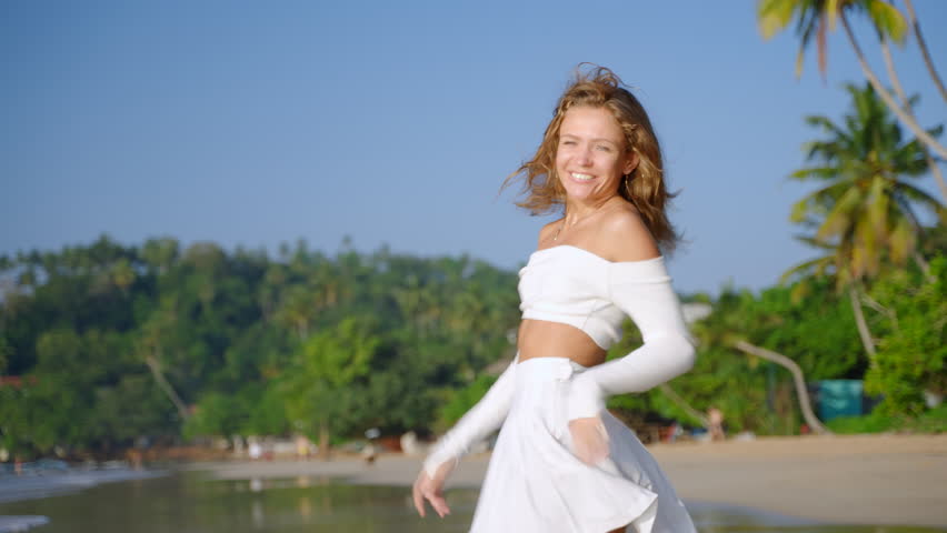 Nice curly model running, flirting at the golden sand at tropical island coast. Young woman smiling, calling at sandy seaside. Sporty girl having fun on summer holidays. Follow me. Slow motion.