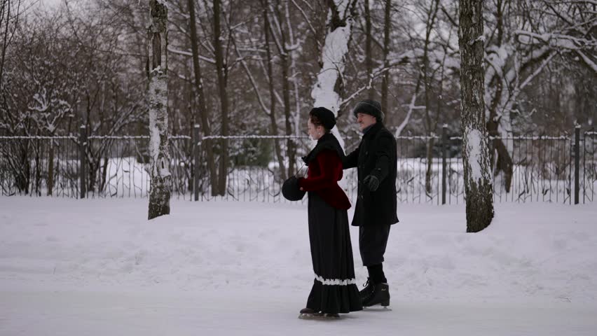 Elegant costumes and antique style emphasize the atmosphere of the 19th century at the skating rink, where a couple holds hands.