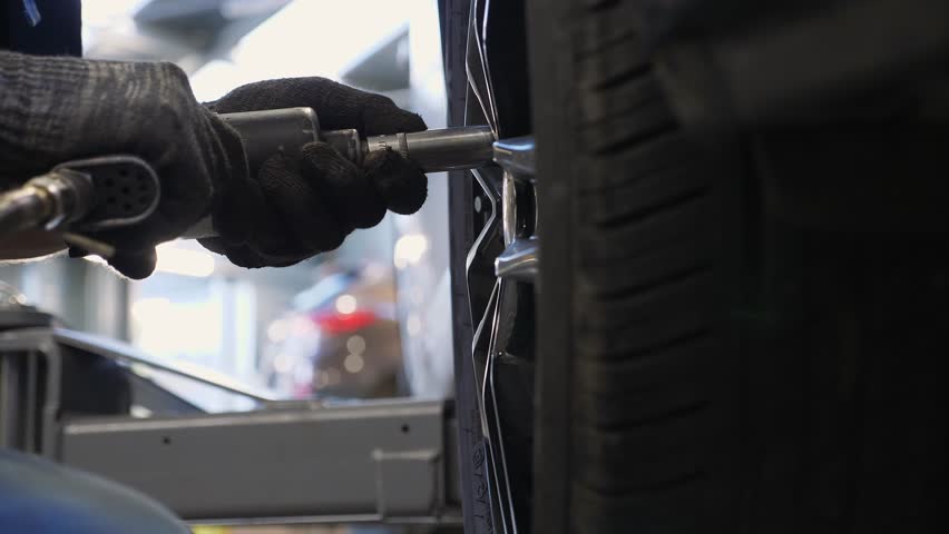 Close-up of the mechanic unscrewing the wheel from the car to the service station, replacing the rubber on the car. Repair of wheels in an auto repair shop.