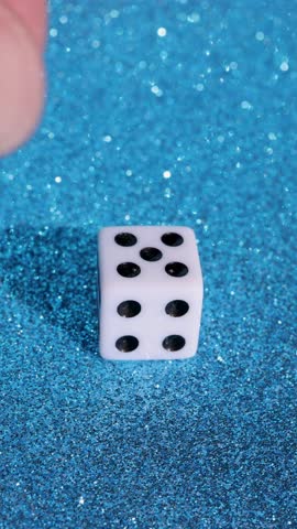 Portrait vertical footage of a man rolling a dice on a blue glittery background showing the number five on the dice 