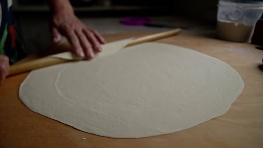 Pastry professional smoothly rolling delicate dough onto wooden pin, revealing precise culinary technique in professional kitchen setting