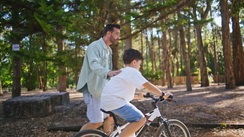 Small son learning cycling at summer sunny urban park. Adorable kid spending time with dad enjoying bicycle sport. Little boy driving cycle with father help. Recreation hobby leisure weekend concept