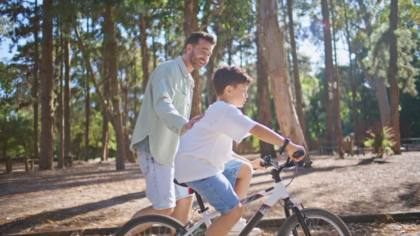 Small son learning cycling at summer sunny urban park. Adorable kid spending time with dad enjoying bicycle sport. Little boy driving cycle with father help. Recreation hobby leisure weekend concept