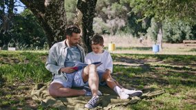 Young father reading fairytale for son in cozy garden. Man parent and kid boy resting on blanket enjoying book. Caring daddy and child bonding spending morning together. Family lifestyle concept  - Powered by Shutterstock - Get 15% off with code: PIKWIZARD15