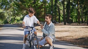Caring dad teaching son bike ride at sunshine park zoom on. Brunette bearded father talking small kid explaining how to riding bicycle at greenery urban forest. Man boy communicating together at alley - Powered by Shutterstock - Get 15% off with code: PIKWIZARD15