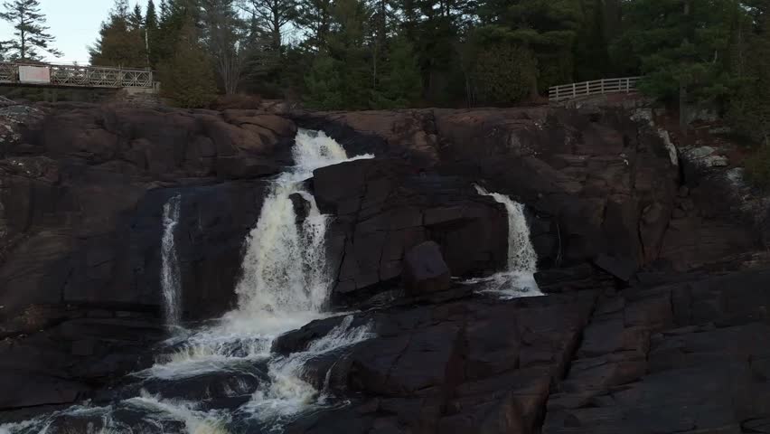 A drone zoom out revealing high cascading waterfalls in High Falls Park, Bracebridge, Ontario, Canada, during evening